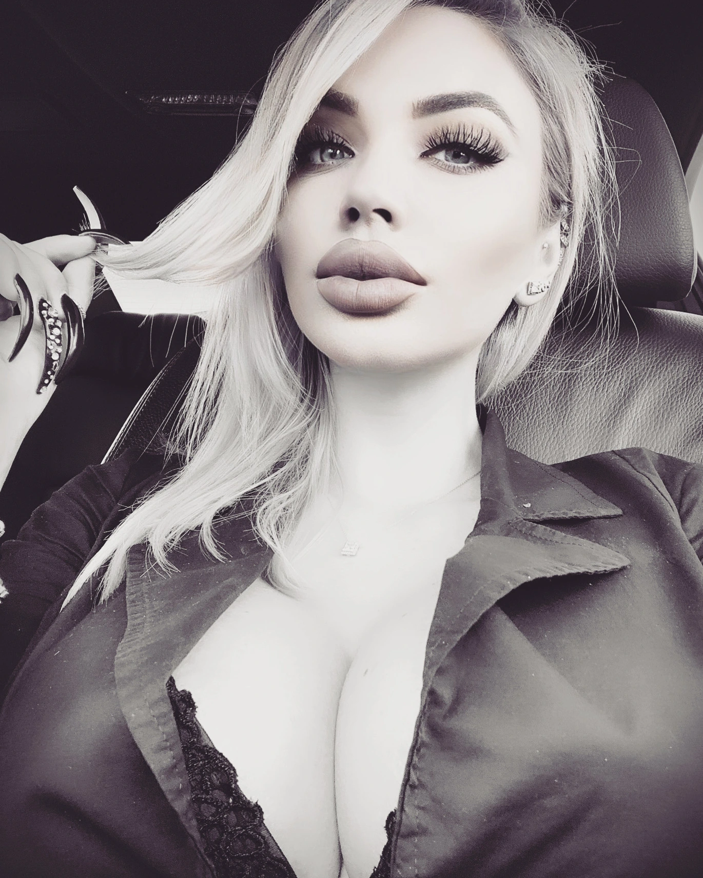 A black-and-white portrait of Sasha in the car, her long platinum hair swept aside by a hand with long dark nails, in an open shirt over black lace.