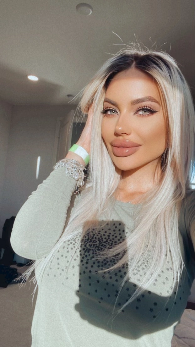 Sasha in a sage top with her hair pushed back, lit by the afternoon sun at home.
