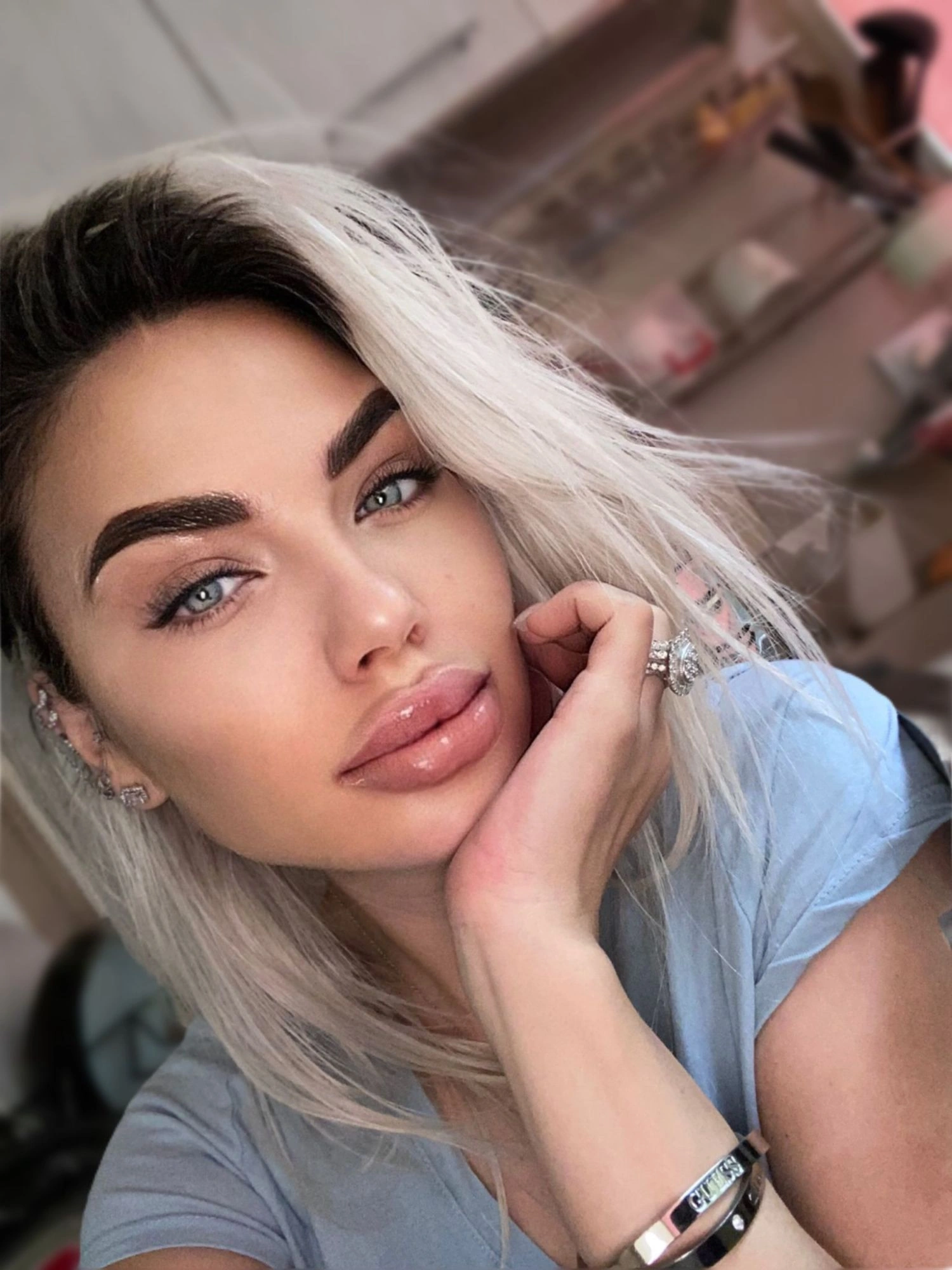 Sasha in a sky-blue tee, her chin resting on her hand, with a big diamond ring.