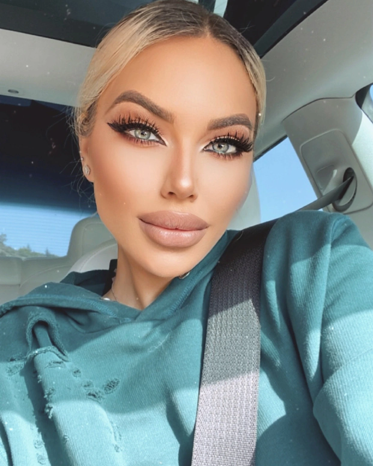 A sunny selfie in the car: Sasha in a teal hoodie, her hair pulled back and her seat belt on.