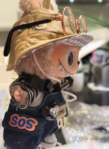 Labubu Nº 14: a gold bucket hat with round glasses and SOS overalls.